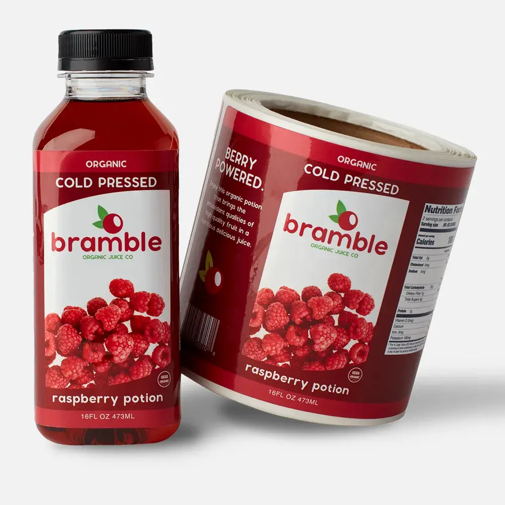 Bramble Organic Juice glossy roll labels displayed beside a raspberry juice bottle with the applied custom label.