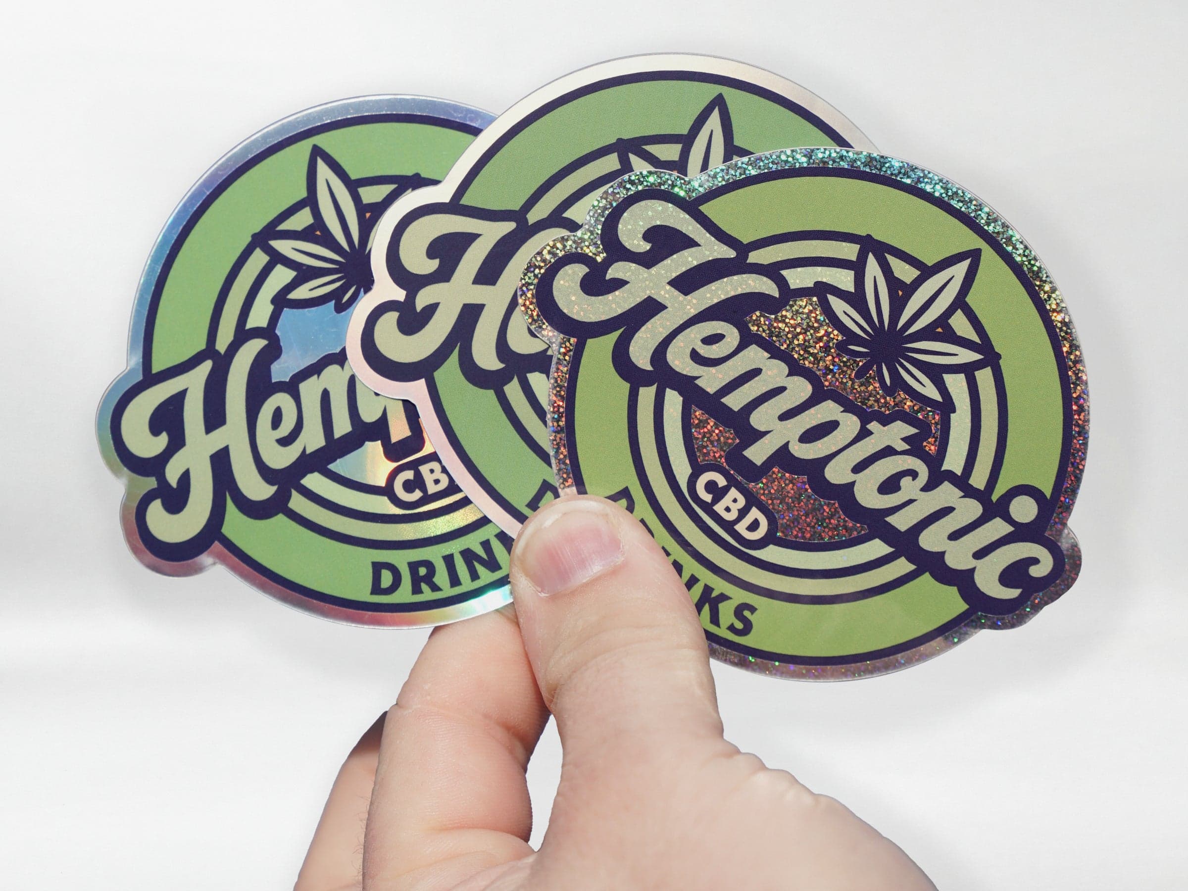 Holographic CBD logo stickers with multiple specialty finishes displayed in hand.