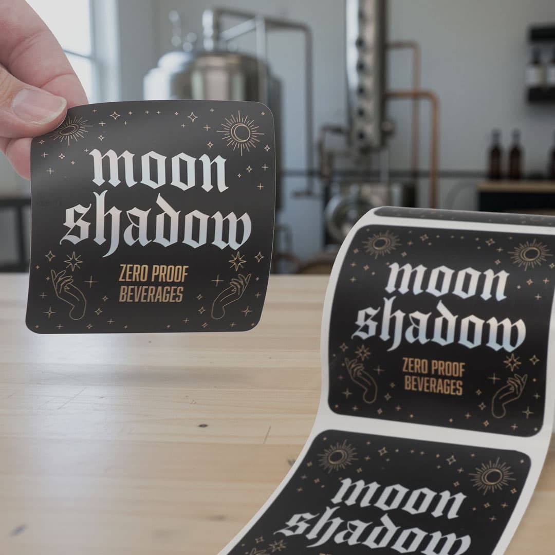 Hand peeling a Moon Shadow custom kiss cut roll sticker in a beverage production facility.