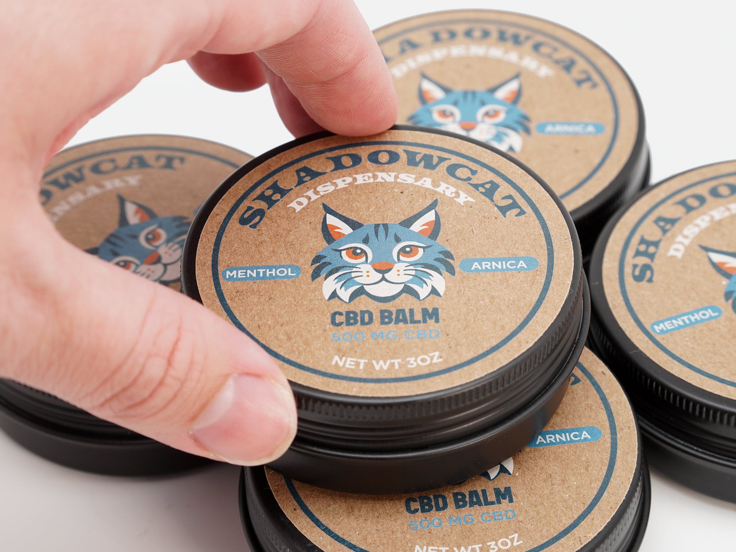 Kraft paper CBD balm labels applied to round product tins with a hand removing the lid.