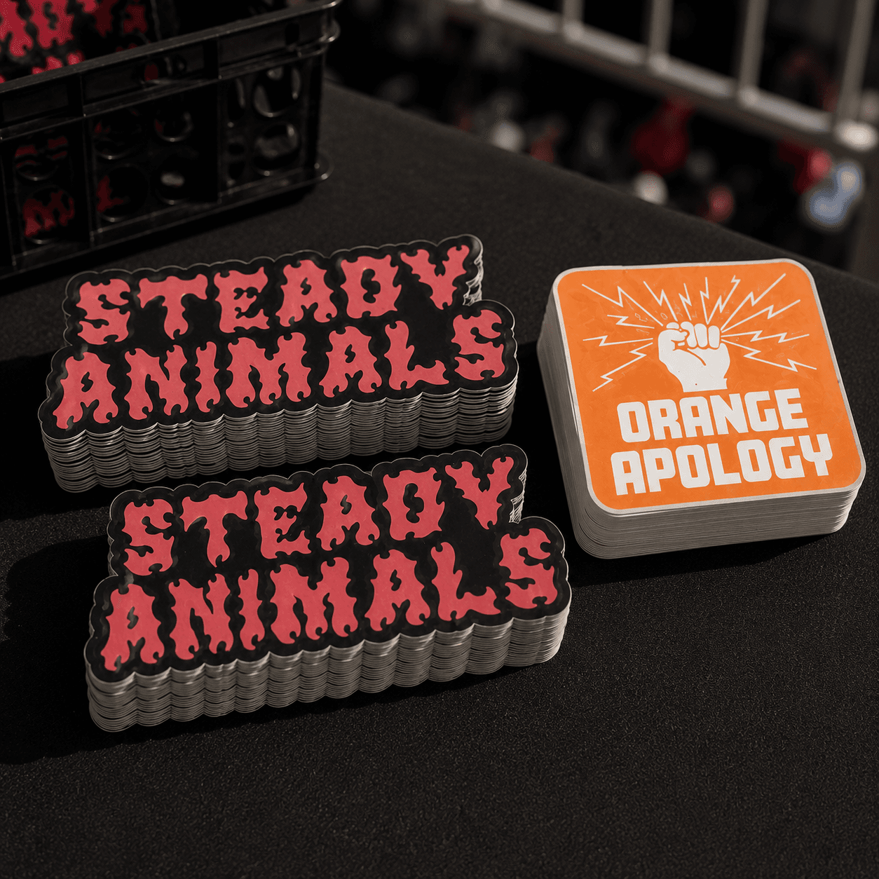 Custom band stickers displayed on a concert merch table with stacks of die cut and square stickers ready for fans to purchase.