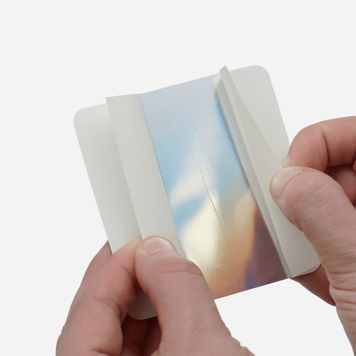 Hands demonstrating the split backing on a holographic sticker, showing the easy peel liner for simple application.