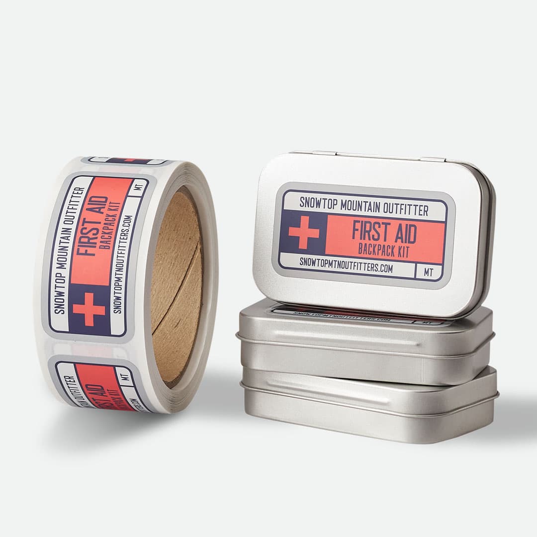 Snowtop Mountain Outfitter matte roll labels applied to first aid kit tins with a matching roll of custom labels.
