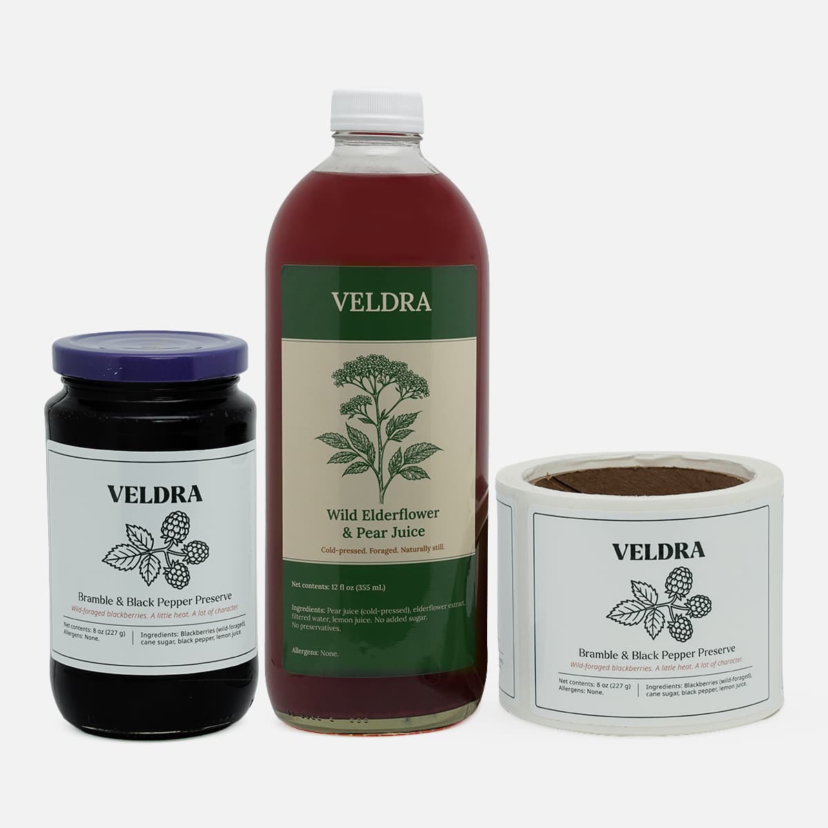 Custom product labels applied to a juice bottle and jam jar alongside a roll of matching labels for a specialty food brand.