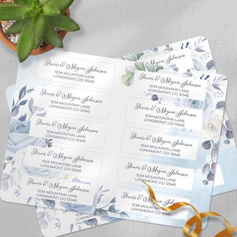Floral return address label sheets with scripted names and addresses displayed beside a small succulent plant.