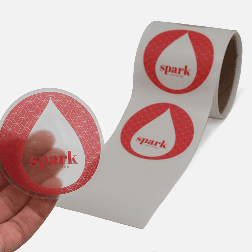 Hand peeling a clear Spark Fizzy Water label from a roll for product application.