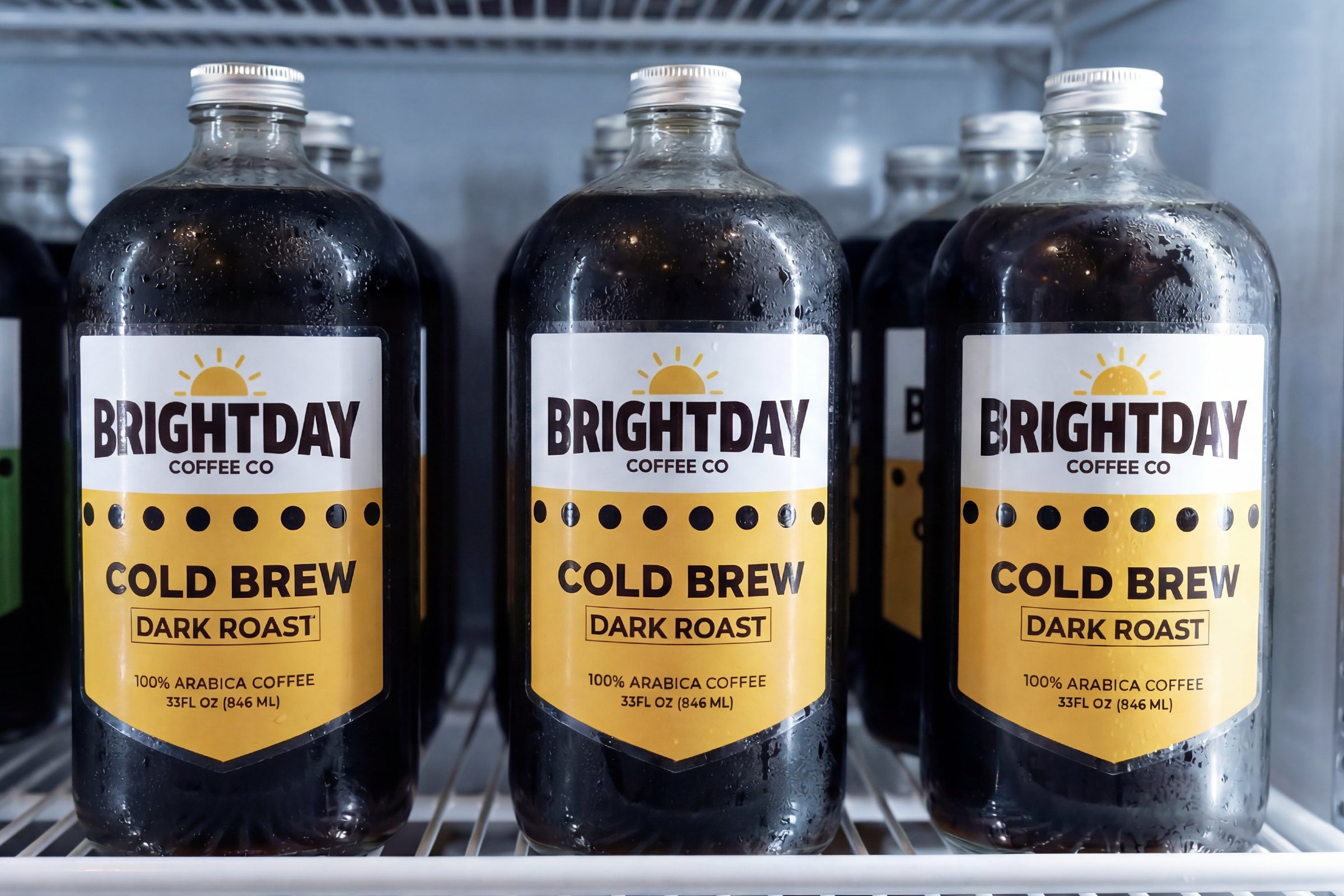 Cold brew coffee bottles with custom product labels displayed in a refrigerator.