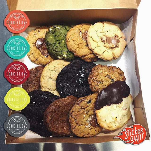 A bakery box filled with assorted cookies in various flavors, shown alongside CookieLove branded rolled labels and a StickerGiant logo.