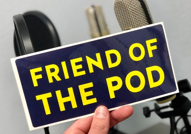 Hand holding a rectangular “Friend of the Pod” sticker in front of two podcast microphones.