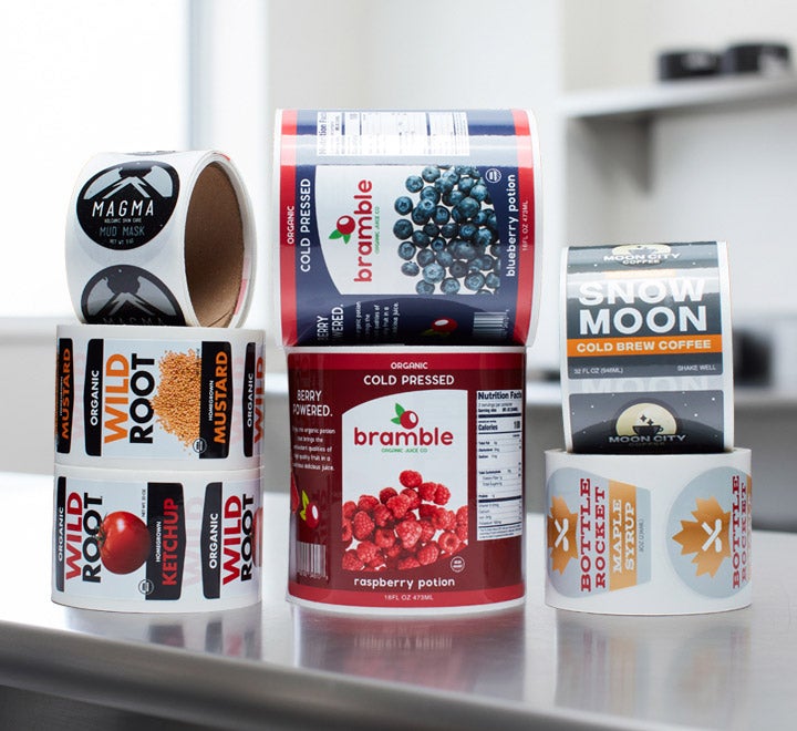 Assorted custom product labels on rolls, displayed upright&mdash;including designs for juice, condiments, coffee, skincare, and syrup.