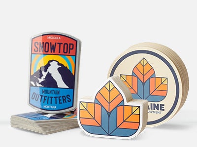 Three die-cut stickers displayed a Snowtop Mountain Outfitters badge design, an orange-and-blue geometric leaf sticker, and a round sticker reading Alpine Equipment.