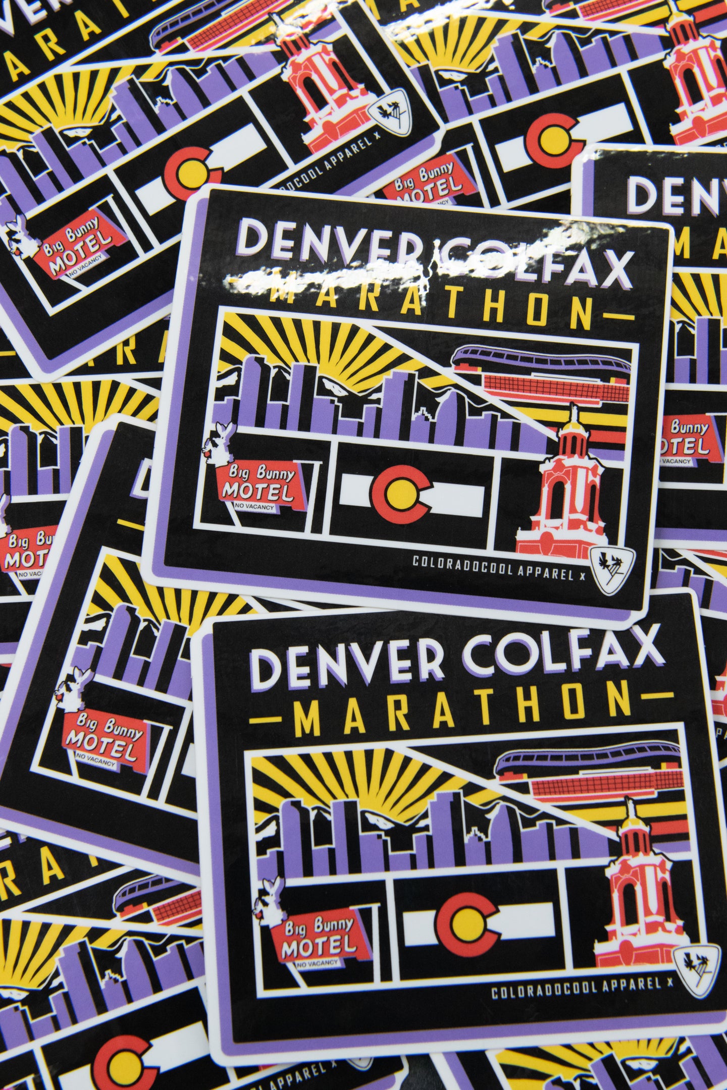 Stacked glossy stickers featuring a &ldquo;Denver Colfax Marathon&rdquo; design with a sunrise skyline, Colorado flag, trolley, and Big Bunny Motel graphic.