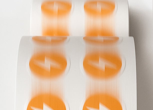 Custom orange logo labels printed on a roll in motion.