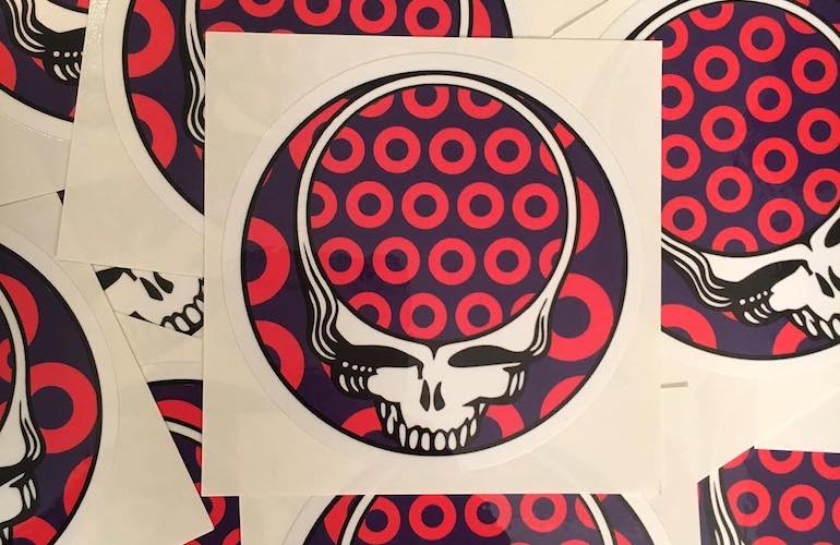 A circular sticker design featuring a stylized white skull with an open top, filled by a pattern of red donut-shaped circles on a dark purple background.