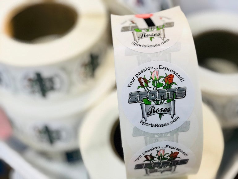 Roll of custom Kiss Cut Stickers for Sports Roses featuring their circular logo on durable BOPP material, used for branding and packaging.