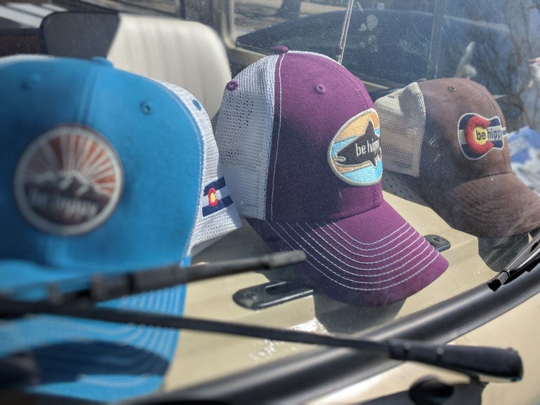 Four Be Hippy trucker hats displayed on a vehicle dashboard, each featuring different embroidered patch designs inspired by Colorado and the outdoors.