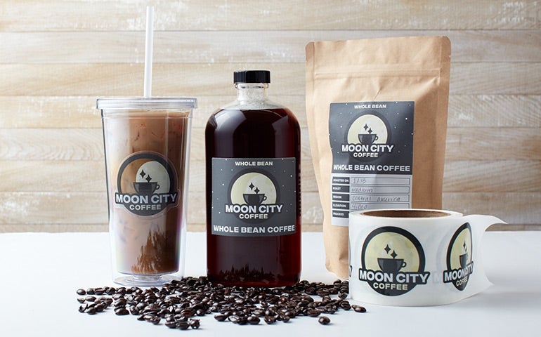 Moon City Coffee cups, bottle, kraft bag, and label roll with branded labels.