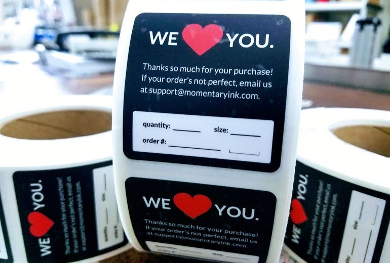 Roll of custom Matte Labels for Momentary Ink featuring a ‘We Love You’ message, customer support information, and writable fields for quantity, size, and order number.