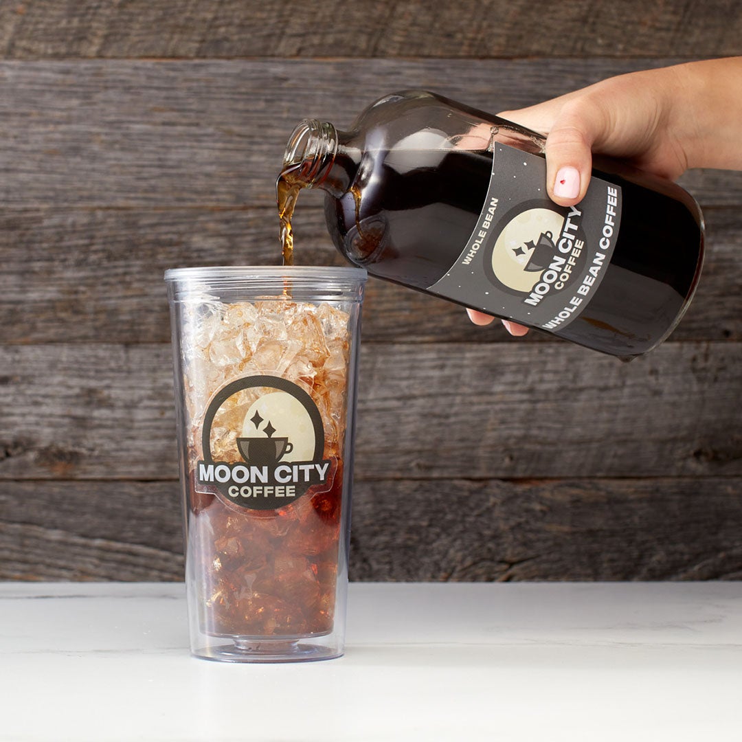 Custom clear label with Moon City Coffee logo applied to a glass bottle and cup in a coffee pouring scene.