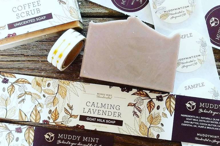 Muddy Mint soap surrounded by branded product labels and samples arranged on a wooden surface.