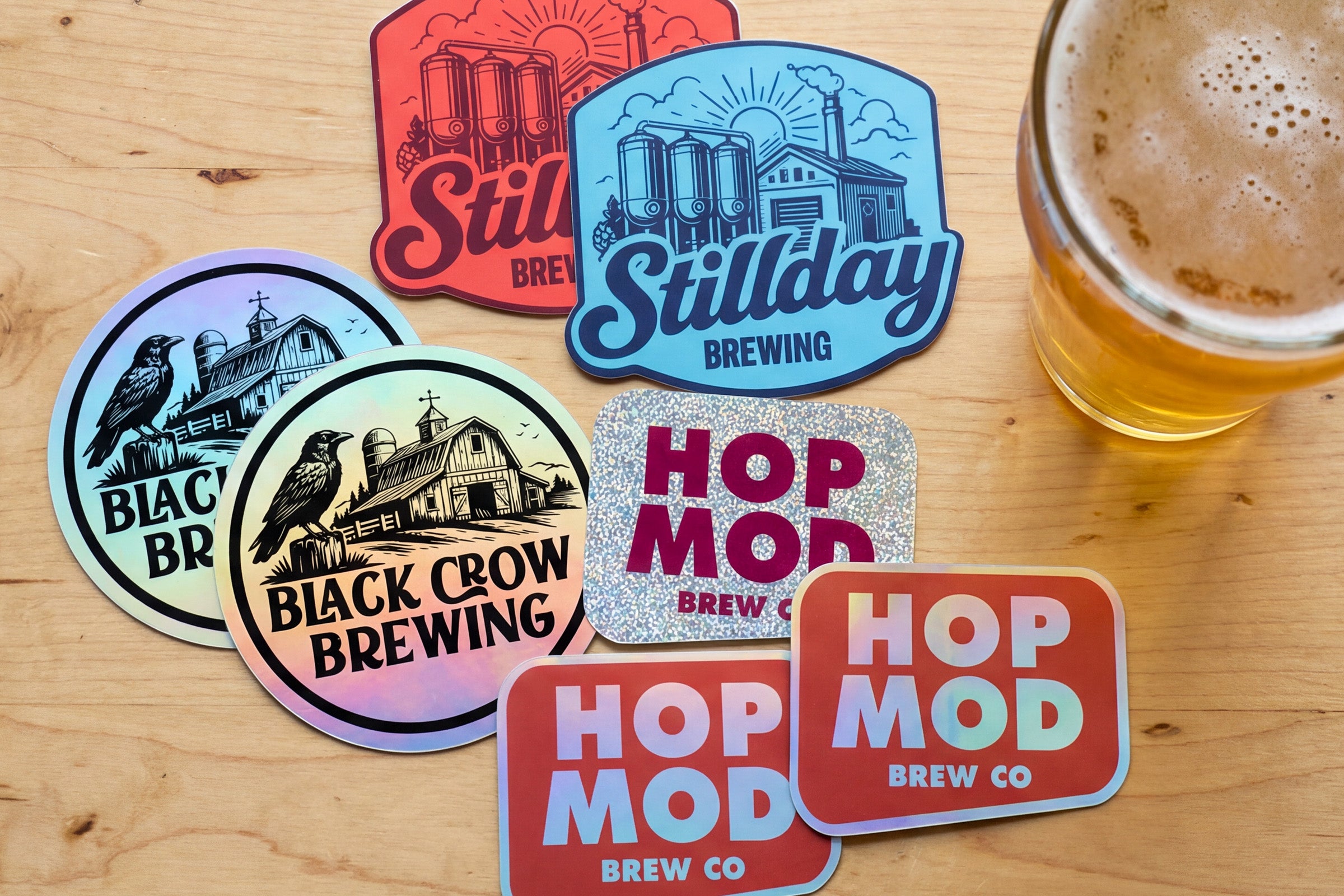 Custom brewery logo stickers in multiple finishes displayed next to a glass of beer.